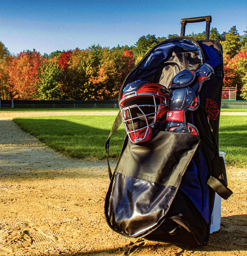 Rango Sports Clubhouse custom baseball bag on a field, full of the catcher’s equipment. The bag has rolling wheels and extra storage