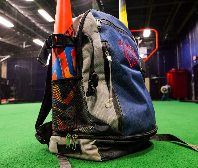 Rango Sports custom baseball bag with two bats, shown on indoor turf field, featuring team logo embroidery and durable design.