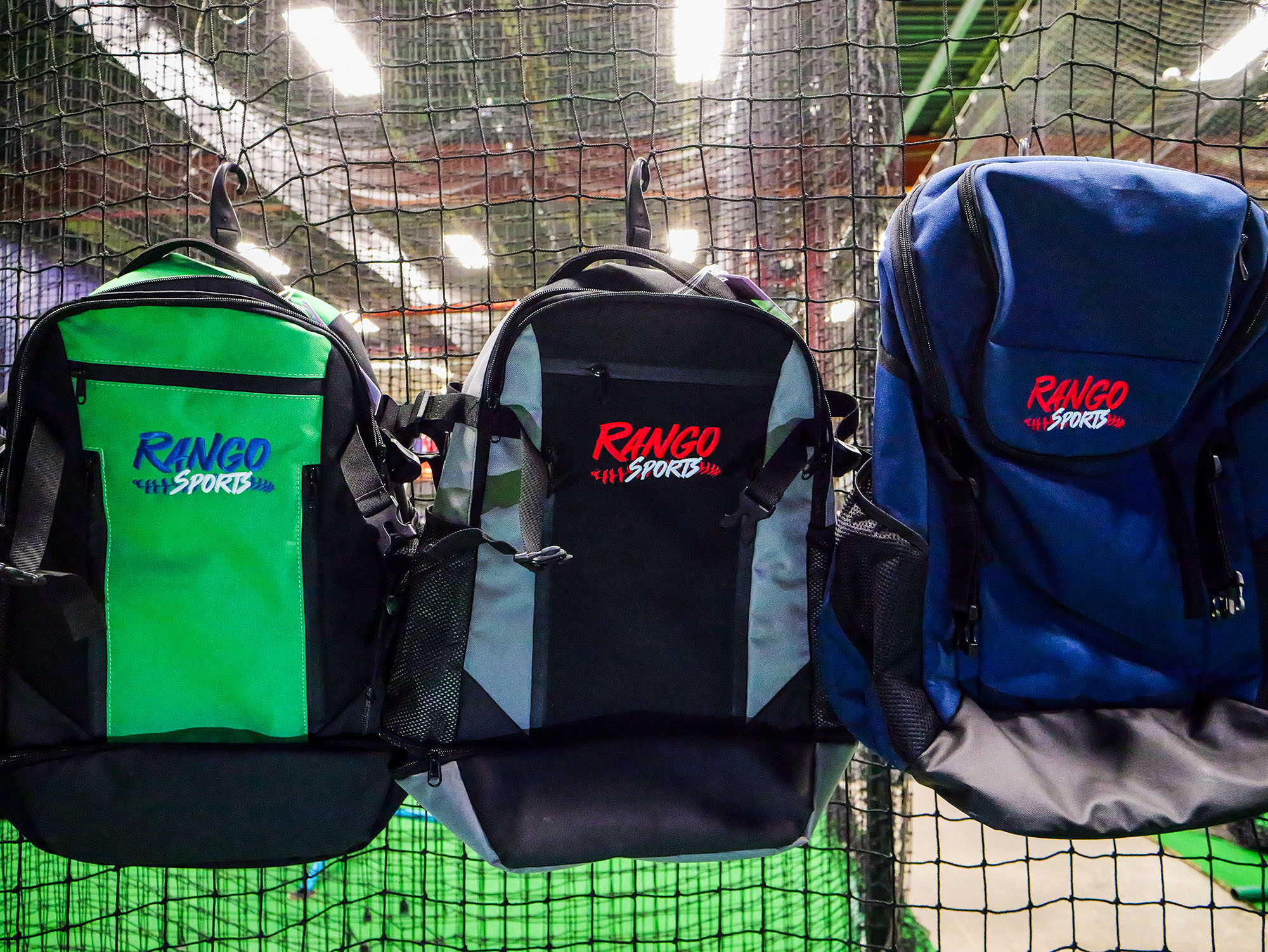 3 baseball bags with Rango Sports logos hanging on a fence