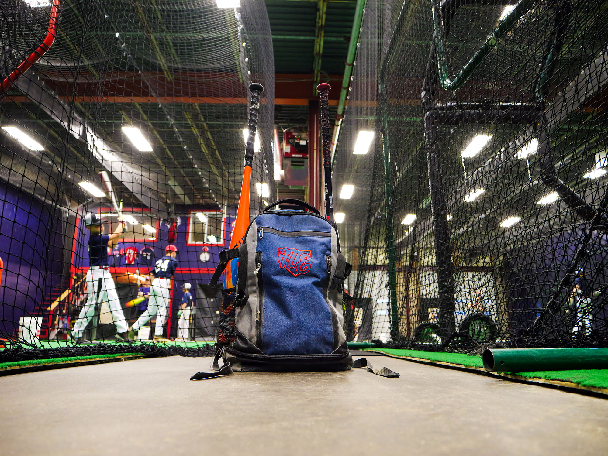 Custom Rango Sports baseball bag with bats inside an indoor batting cage.